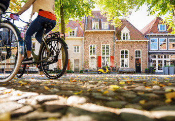 Deux personnes à vélo passent devant un hébergement de glamping charmant et des maisons colorées sur pavés.