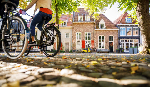 Dos personas pasean en bicicleta junto a alojamientos glamping encantadores y casas de colores sobre adoquines.