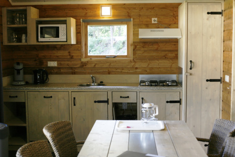 Cocina revestida de madera en Safarilodge deluxe de Familievakantiepark Krieghuusbelten, Países Bajos, equipada con estufa y microondas.