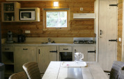 Wood-paneled kitchen in the Safarilodge deluxe at Familievakantiepark Krieghuusbelten, Netherlands, with stove and microwave.