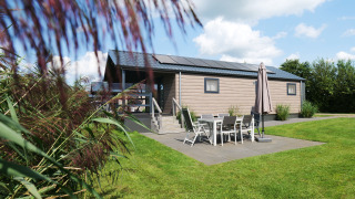 A modern Waterlodge with a patio, outdoor dining set, and umbrella on a green lawn under a blue sky.