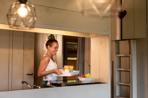 Mujer sirviendo desayuno con jugo en la cocina de una lujosa tienda safari en Familievakantiepark Krieghuusbelten.