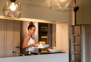 Donna che serve la colazione con succo nella cucina di una tenda safari di lusso al Familievakantiepark Krieghuusbelten.