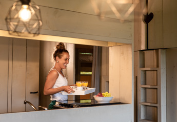 Donna che serve la colazione con succo nella cucina di una tenda safari di lusso al Familievakantiepark Krieghuusbelten.