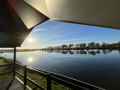 Vue depuis Waterlodge au Familievakantiepark Krieghuusbelten aux Pays-Bas, soleil et lac en reflet.
