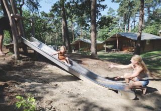 Enfant descendant un toboggan vers une femme devant la tente Safarilodge deluxe aux Pays-Bas.