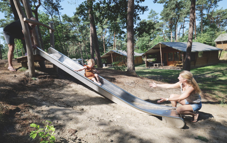 Enfant descendant un toboggan vers une femme devant la tente Safarilodge deluxe aux Pays-Bas.
