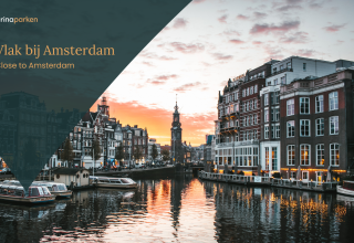 Puesta de sol sobre un canal cerca de Ámsterdam, con barcos y edificios históricos junto al agua.