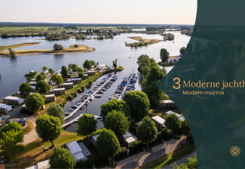 Aerial view of a modern marina with glamping lodges and boats on a lake, surrounded by green landscape.