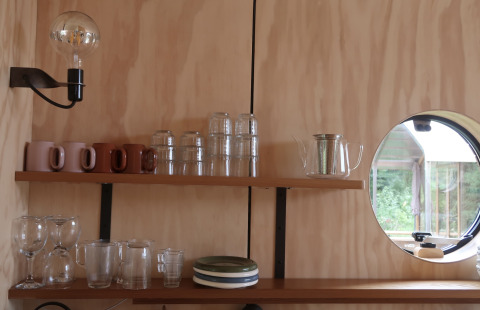 Køkkenhylde i Wrap house med glas, krus, tallerkener og runde vindue på Resort de Parel, Holland.