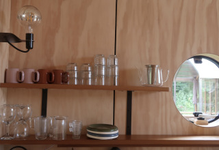 Køkkenhylde i Wrap house med glas, krus, tallerkener og runde vindue på Resort de Parel, Holland.