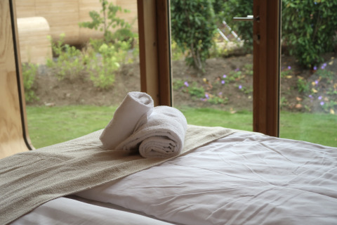 View from Wrap House lodge at Resort de Parel, Netherlands, with towels on the bed and garden outside.