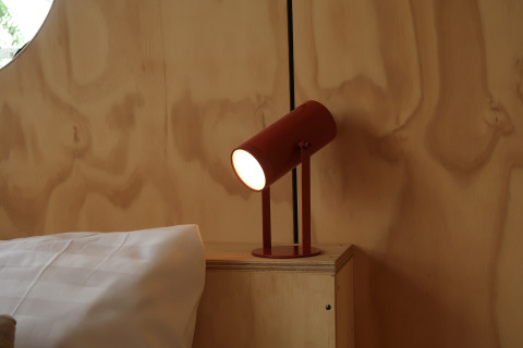 Moderne rode tafellamp op nachtkastje bij het bed in de Wrap House van Resort de Parel, Nederland.