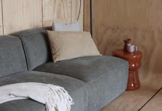 Divano grigio moderno con cuscini e plaid, tavolino con tazza e vaso, Wrap house al Resort de Parel.