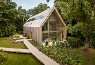 Moderne lodge met grote ramen en houten buitenkant, gelegen in een bosrijke omgeving met wandelpad.