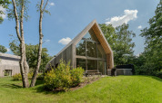 Moderne lodge met grote glaspartijen en jacuzzi, omgeven door natuur en bomen op een zonnige dag.