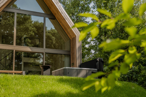 Moderne lodge met grote ramen en een jacuzzi buiten, omringd door groene natuur en bomen.