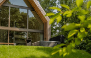 Moderne lodge met grote ramen en een jacuzzi buiten, omringd door groene natuur en bomen.