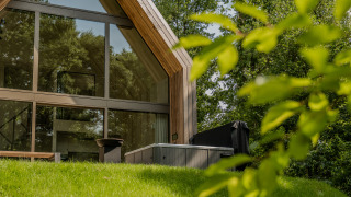 Moderne lodge met grote ramen en een jacuzzi buiten, gelegen tussen weelderig groen en bomen.