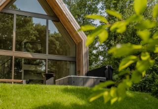 Moderne lodge met grote ramen en een jacuzzi buiten, omringd door groene natuur en bomen.