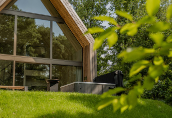 Moderne lodge met grote ramen en een jacuzzi buiten, omringd door groene natuur en bomen.