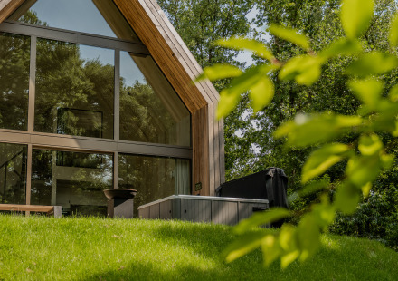 Moderne lodge met grote ramen en een jacuzzi buiten, gelegen tussen weelderig groen en bomen.