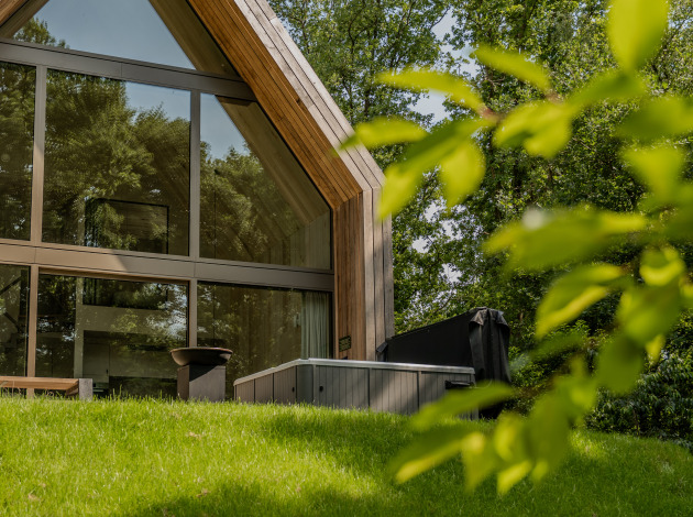 Moderne lodge met grote ramen en een jacuzzi buiten, gelegen tussen weelderig groen en bomen.