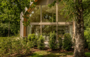 Moderne lodge met grote glaspartijen, omgeven door weelderig groen en bomen in een bosrijke omgeving.