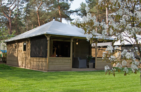 Outdoor view of Kampeerlodge featuring a wooden structure, covered terrace, and lush green surroundings.