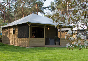 Vue extérieure de la Kampeerlodge avec structure en bois, terrasse couverte et environnement verdoyant.