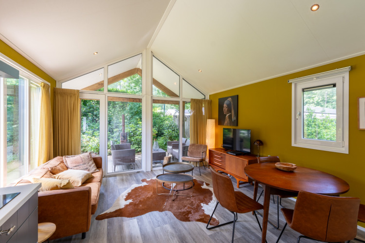 Salón moderno en Eco Cottage, De Thijmse Berg, Países Bajos, con grandes ventanales, sofá y decoración de madera.