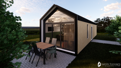 Udendørsbillede af Reestdal Lodge, en moderne hytte med glasfacade og terrasseområde med havemøbler.