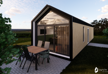 Vue extérieure de la Reestdal Lodge, cabane moderne avec grande baie vitrée et terrasse avec mobilier repas.