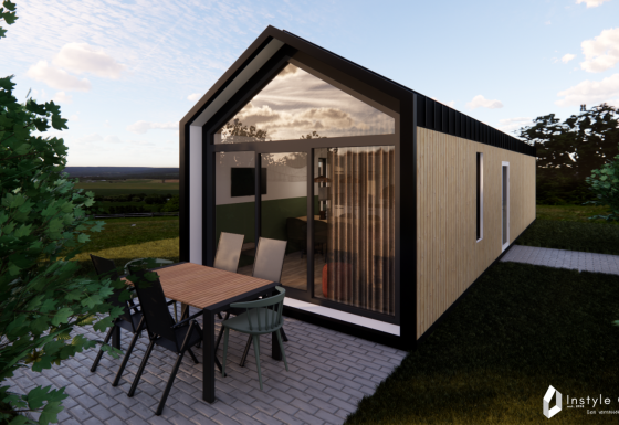 Udendørsbillede af Reestdal Lodge, en moderne hytte med glasfacade og terrasseområde med havemøbler.