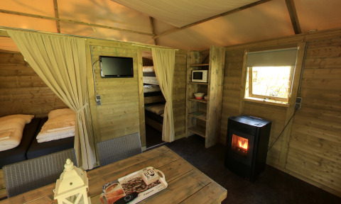 Innenansicht der Kampeerlodge im Familievakantiepark Krieghuusbelten mit Betten, Ofen und Holzwänden.