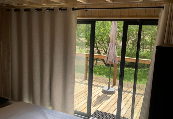 Soveværelse med træloft, store vinduer og udsigt til terrasse og grøn natur ved Cocoon de l'Ourthe, Belgien.