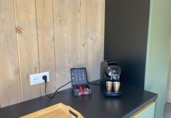 Et kaffehjørne med kaffemaskine, kapsler og kopper på en sort bordplade i Cocoon de l'Ourthe-lodgen.