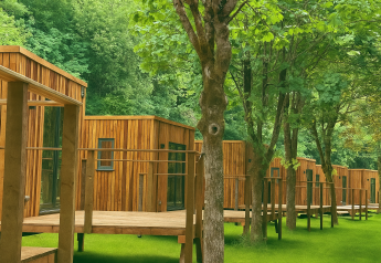 Houten lodges bij Eco Lodge in Hameau de l'Ourthe, België, omgeven door groene bomen en gras.