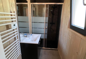 Salle de bain moderne à Eco Lodge avec panneaux en bois, douche vitrée, lavabo et lumière naturelle.