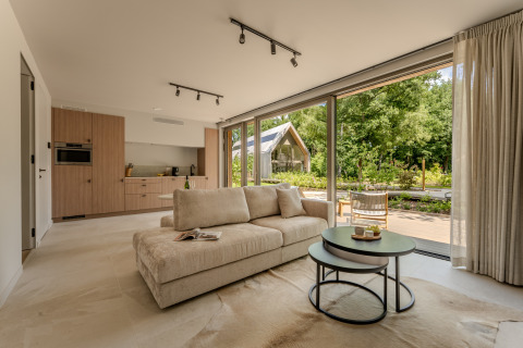 Moderne lodge woonkamer met grote ramen, neutraal interieur en uitzicht op een groene tuin buiten.