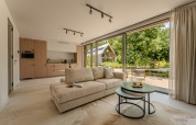 Luxe woonkamer van een lodge met grote ramen, licht interieur en zicht op de groene natuur buiten.