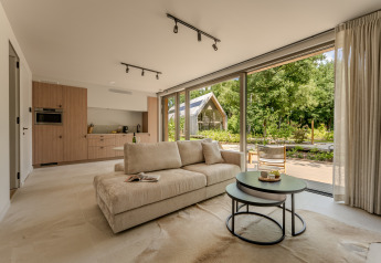 Helles Wohnzimmer einer Lodge mit großen Fenstern, offener Küche und Blick auf einen grünen Garten.
