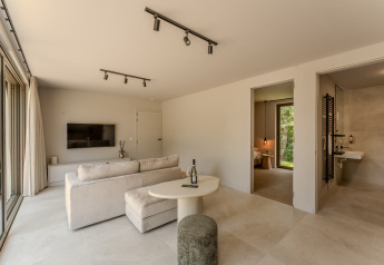 Salon lumineux et moderne de lodge avec accès à la chambre et salle de bain, TV murale et grandes fenêtres.