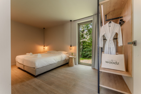 Habitación de lodge moderna con cama doble, lámparas colgantes, bata y gran ventanal con vista al bosque.