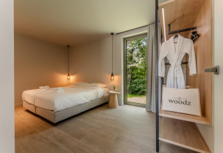 Modernes Lodge-Zimmer mit Doppelbett, offenen Kleiderschrank, Bademantel und Blick ins Grüne.