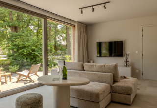 Helles Wohnzimmer in der Suite Accessible der Woodz Lodges, Belgien, mit großem Fenster zur Natur.