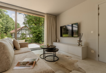 Soggiorno moderno di un lodge con divano grande, TV a parete, vetrata e vista sul giardino esterno.