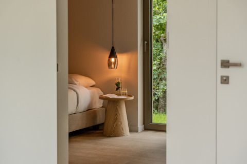 Chambre chaleureuse dans un lodge, avec lampe suspendue, table en bois et vue sur la nature verdoyante.