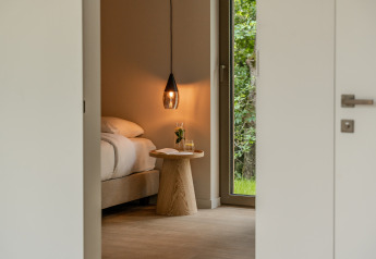 Chambre chaleureuse dans un lodge, avec lampe suspendue, table en bois et vue sur la nature verdoyante.