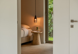 Dormitorio acogedor en una cabaña, con lámpara colgante, mesa de madera y vistas a la naturaleza.